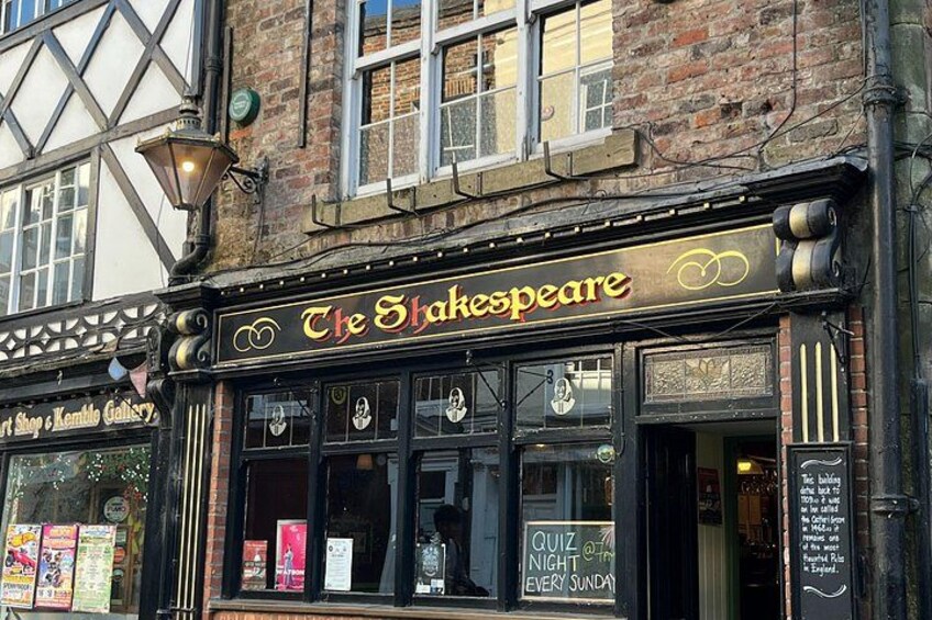 A Shakespeare-themed pub with a sign that reads 'The Shakespeare' and a window display advertising a quiz every Sunday. 3