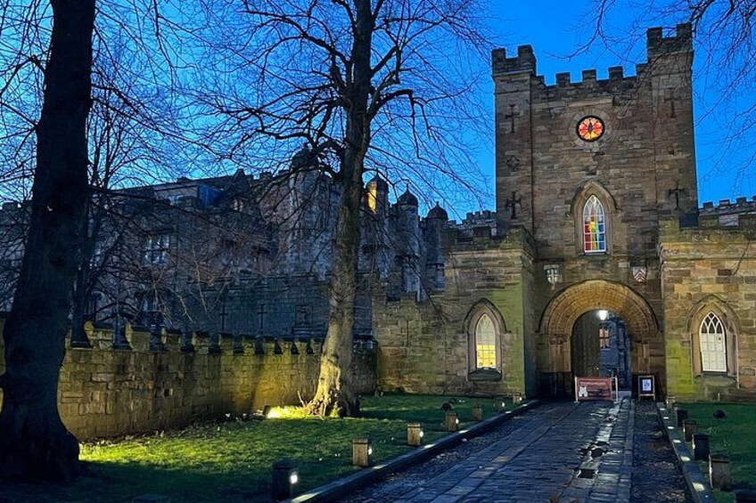 A historic stone building with a clock tower, arched entrance, and a pathway leading to it. 2