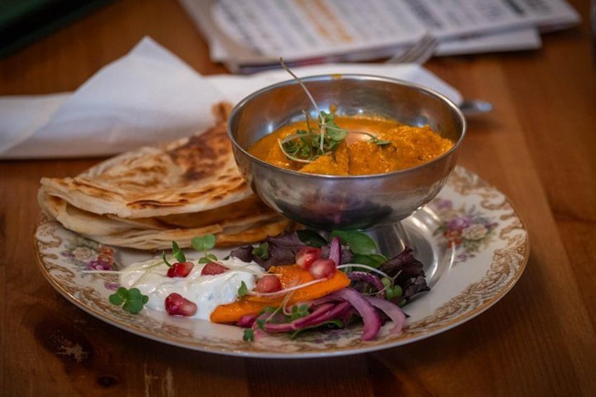 A plate with a bowl of curry, flatbread, and a salad. 5