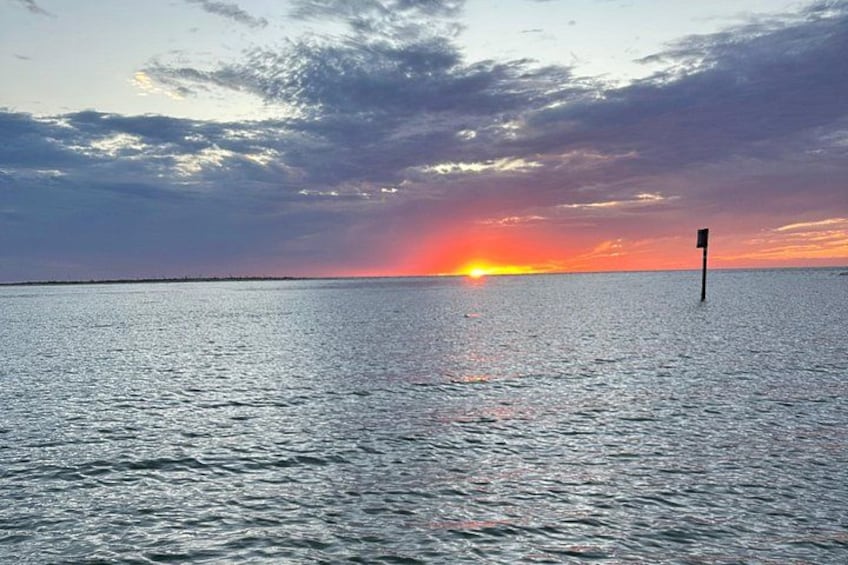 Ein Sonnenuntergang über einem ruhigen Meer mit einem einzelnen Pfahl in der Ferne. 4