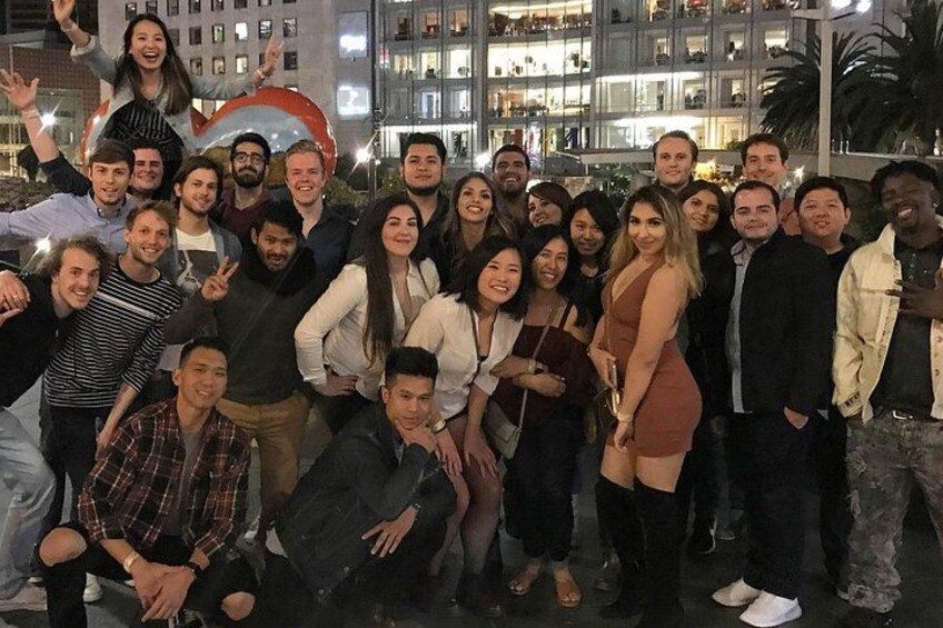 Eine Gruppe von Menschen posiert für ein Foto in einer Stadt, im Hintergrund sind Gebäude und eine große, runde Struktur zu sehen. 5
