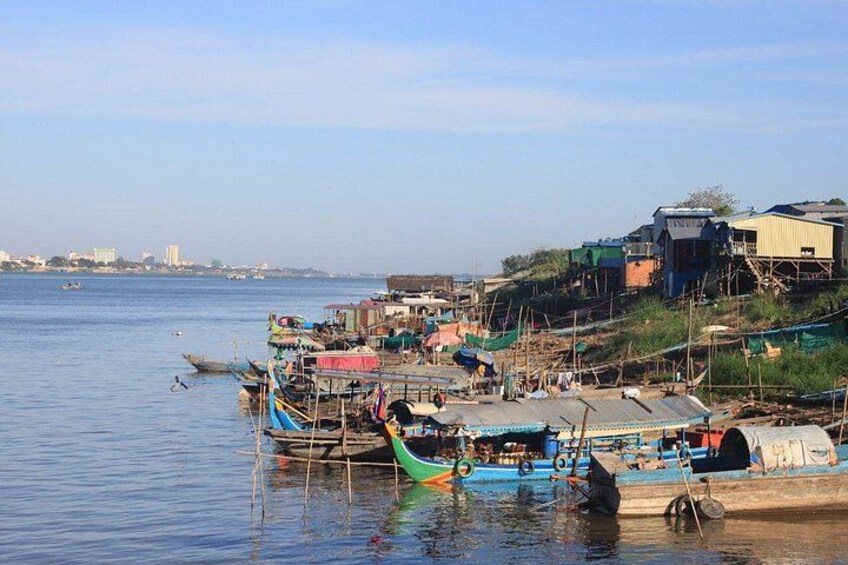 Un asentamiento a orillas del río con barcos amarrados, edificios y un horizonte urbano lejano. 3