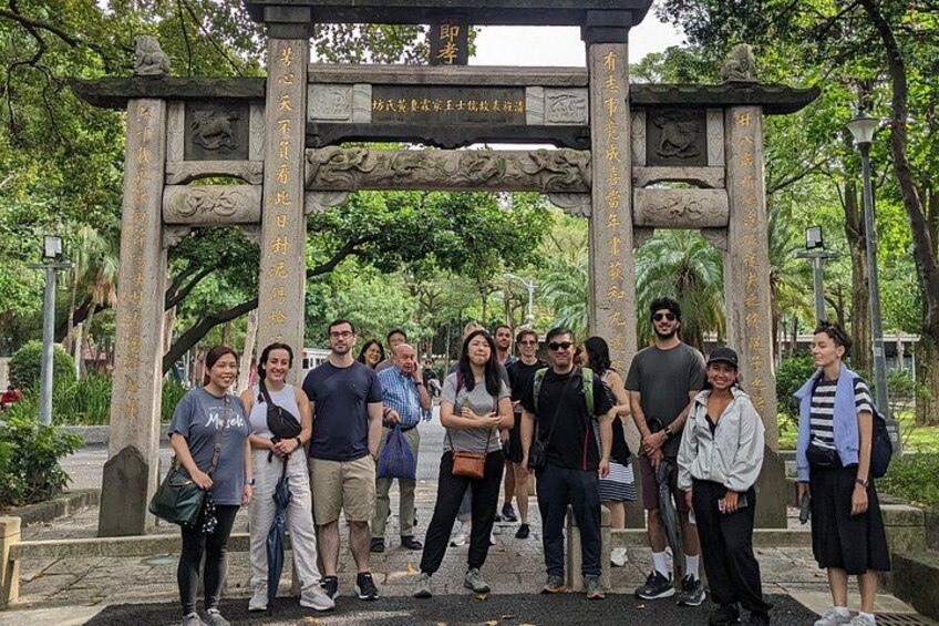 A group of people standing in front of a stone archway with inscriptions. 1