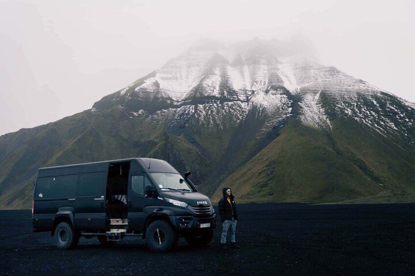 Una camioneta negra estacionada frente a una montaña, con una persona de pie a su lado. 4