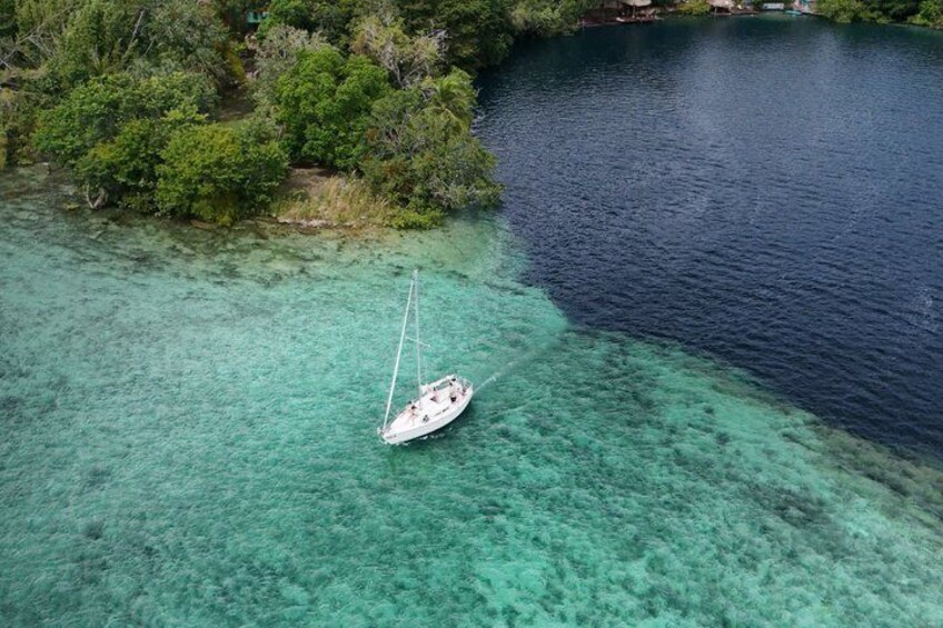 A sailboat anchored in clear turquoise waters, surrounded by lush greenery and a dense forest. 3
