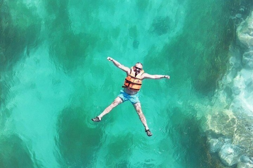 A person floating in clear turquoise water, wearing a life jacket and shorts. 4