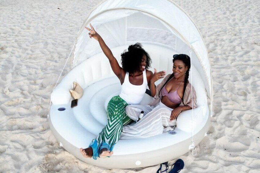 Two people sitting in a white inflatable structure on a sandy beach. 1