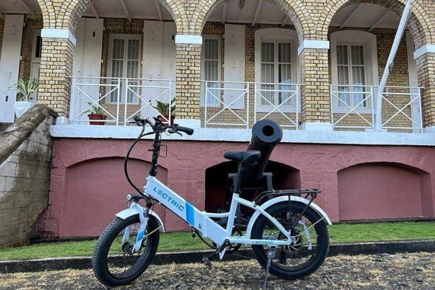 A white electric bicycle parked in front of a building with arched windows and a brick facade. 2