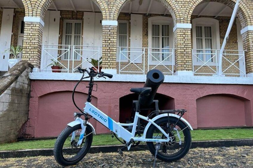 A white electric bicycle parked in front of a building with arched windows and a brick facade. 3