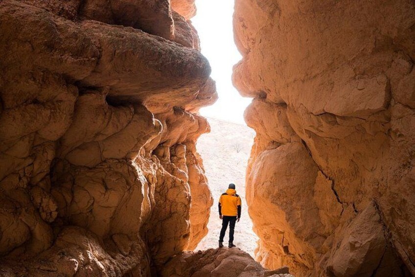 A person in a yellow jacket standing at the entrance of a rock formation. 5
