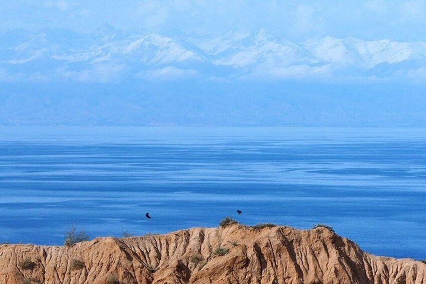 A vast body of water with mountains in the background and a rocky shoreline in the foreground. 2