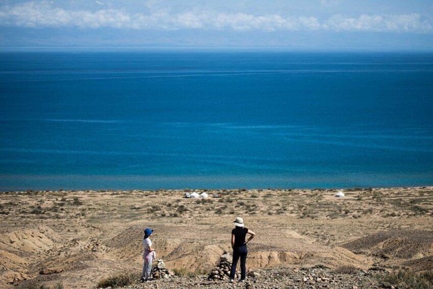 A coastal landscape with a clear blue sea, rocky terrain, and a few white structures. 4