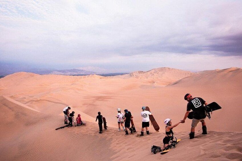 A group of people hiking in a desert with sand dunes and a cloudy sky. 3