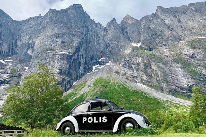 Un'auto della polizia d'epoca con la scritta 'POLIS' sul fianco, parcheggiata di fronte a un paesaggio montuoso. 2