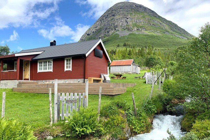 Una casa rossa con una veranda in legno, una montagna sullo sfondo e un piccolo ruscello in primo piano. 5