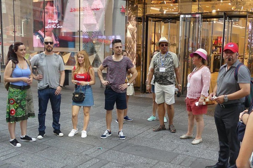 A group of people standing on a sidewalk in front of a store with glass doors. 2