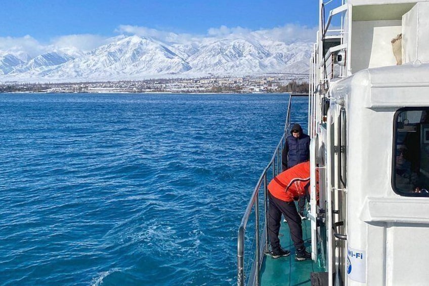 A person in a red jacket on a boat, a snowy mountain range in the background, and calm blue water. 5
