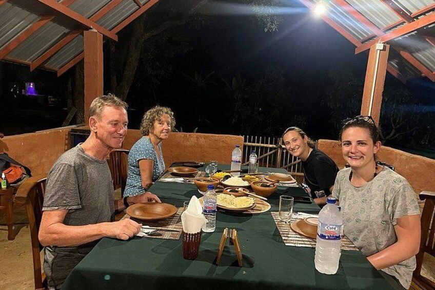 Un groupe de personnes dînant en plein air, de nuit, autour d’une table dressée pour le repas. 2