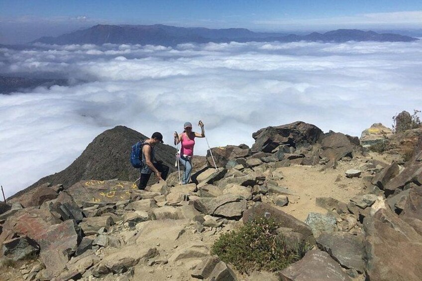 Twee wandelaars op een rotsachtige bergtop, met een uitzicht op wolken. 2