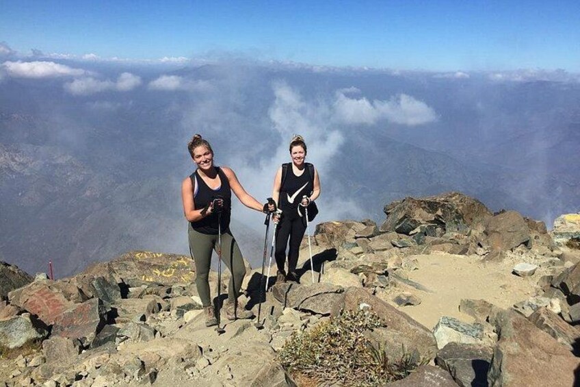Twee mensen wandelen op een rotsachtige bergtop, met een uitzicht op bewolking. 4