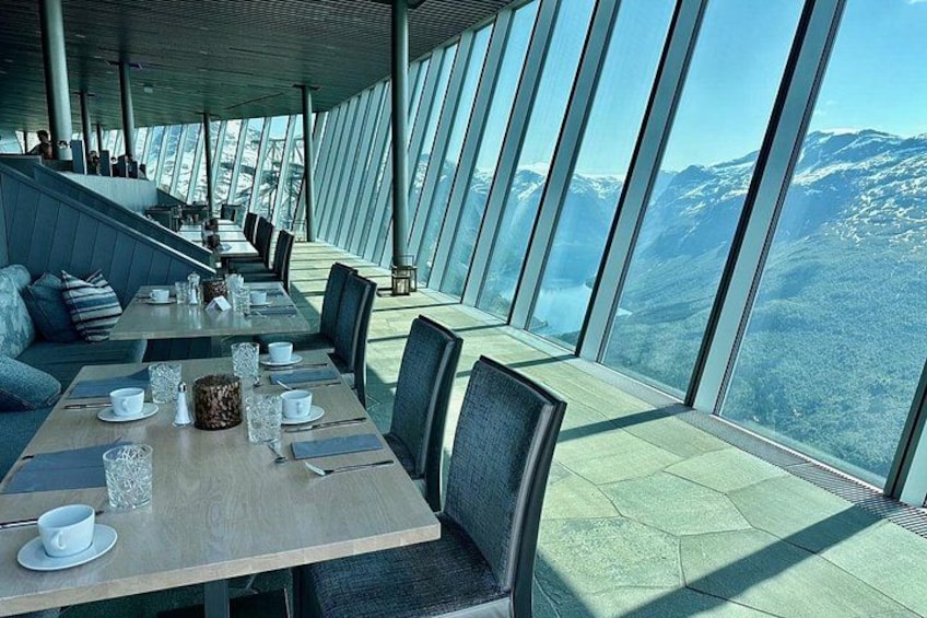 A restaurant with tables and chairs, large windows, and a mountainous landscape view. 2