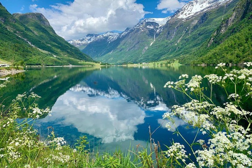 A calm lake surrounded by green mountains and snow-capped peaks under a partly cloudy sky. 4