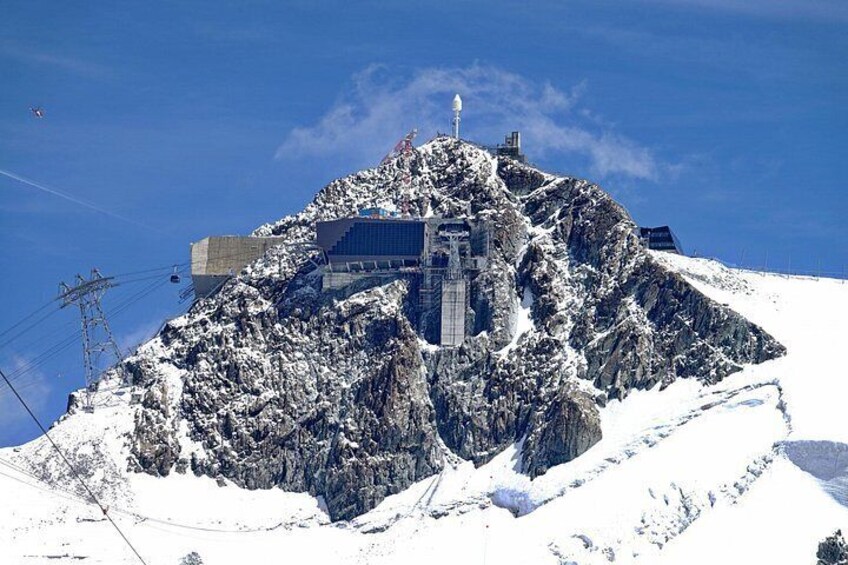 A snow-covered mountain with a building on top, ski lifts, and a clear blue sky. 3