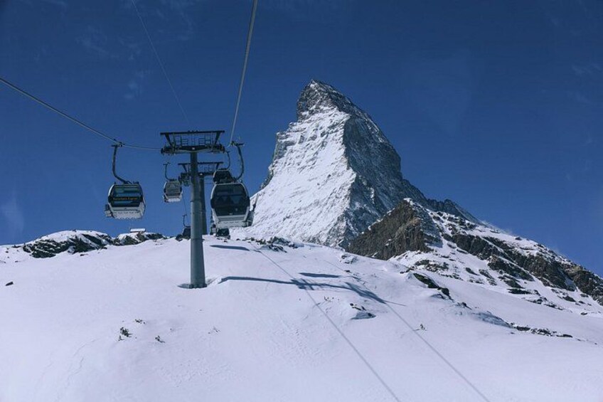 A ski lift with chairs, a snow-covered mountain peak, and a clear blue sky. 3