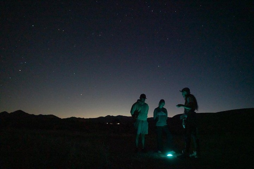 Tres personas de pie en una colina bajo un cielo nocturno estrellado. 2
