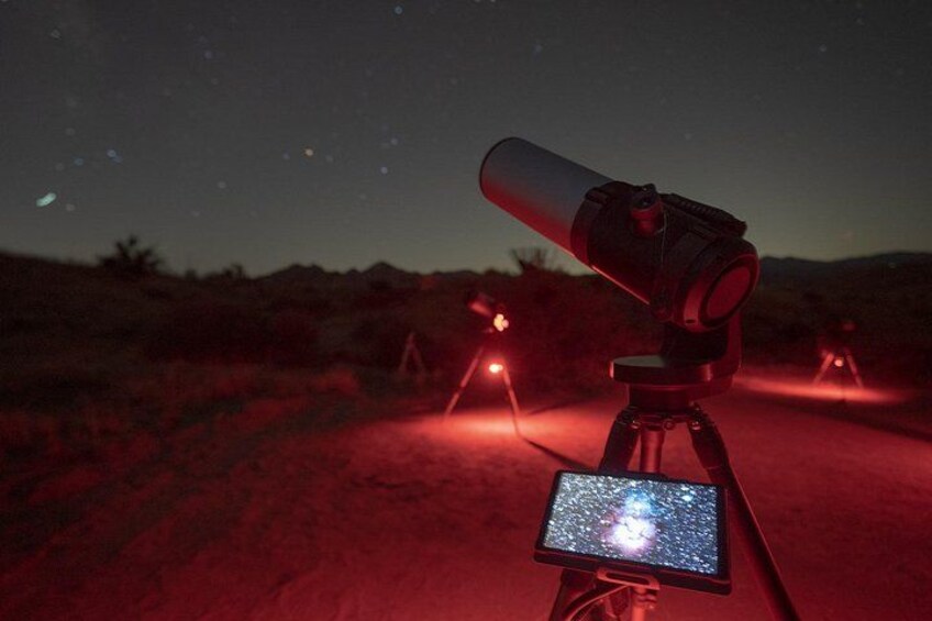 Ein Teleskop auf einem Stativ mit einem Sternenhimmel-Bildschirm, vor einer Wüstenlandschaft bei Nacht. 4