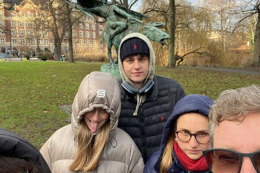 A group of people in a park with a statue and buildings in the background. 4