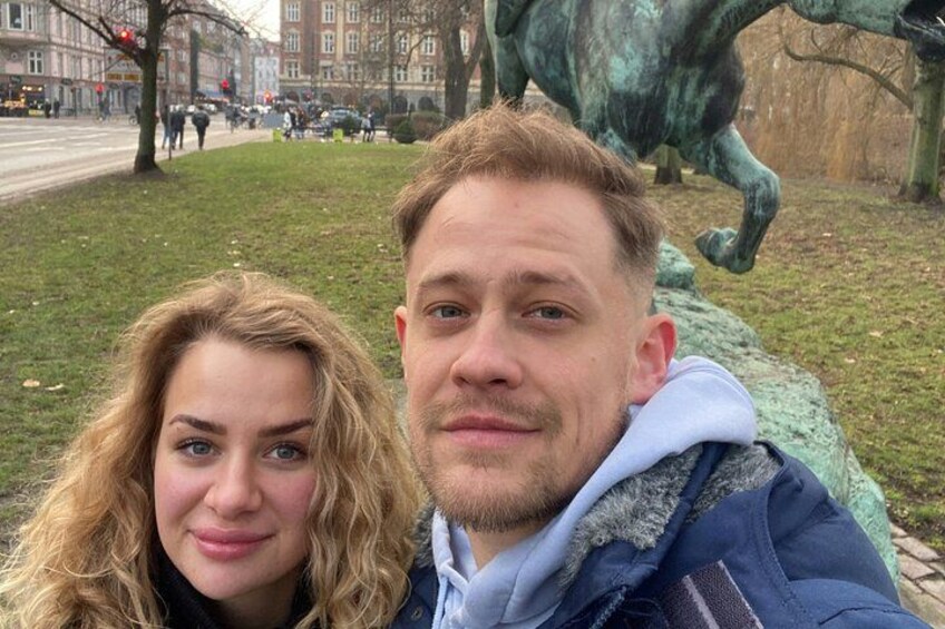 A person in a blue jacket with a fur-lined hood, a woman with curly hair, and a bronze statue of a horse in the background. 2