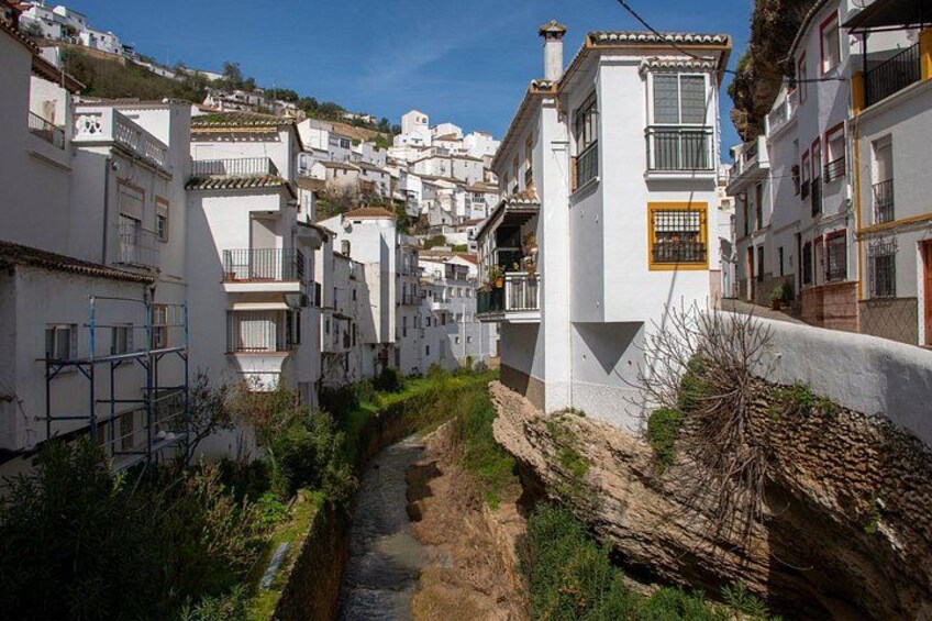 Une rue étroite bordée de bâtiments blancs dotés de balcons, un lit de rivière asséché et, au loin, une colline. 5