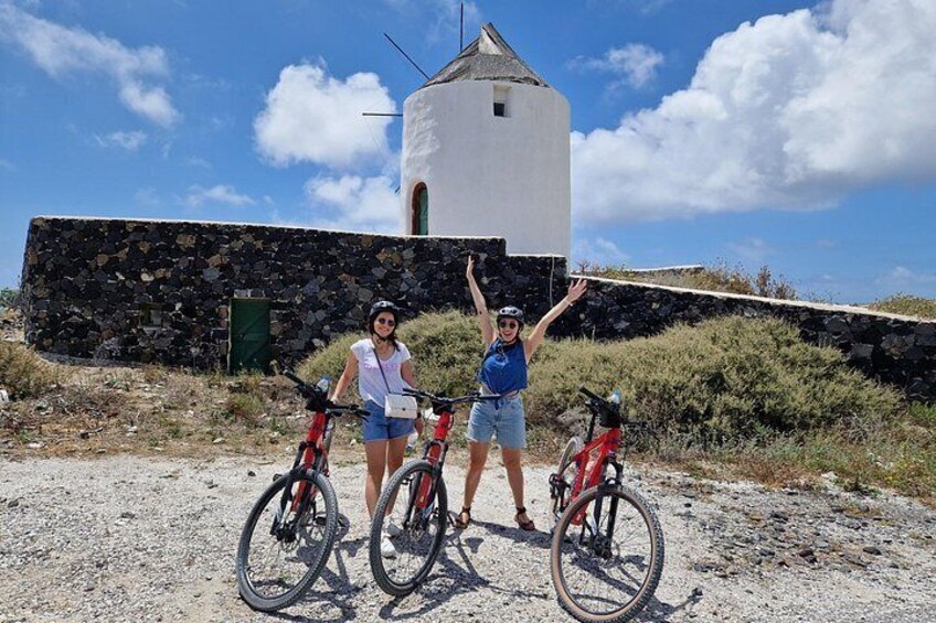 Two people with bicycles in front of a white tower with a stone base. 5