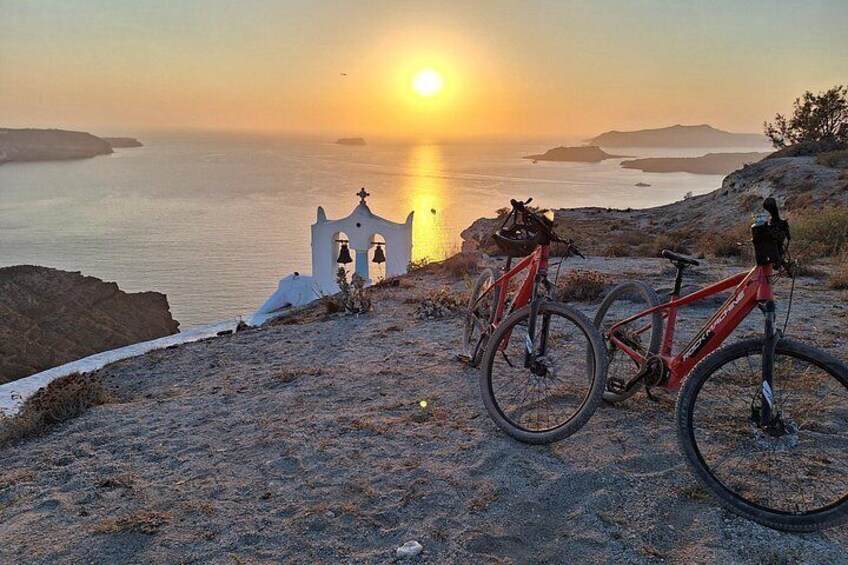 A sunset over the sea, a white bell tower, and two bicycles. 3