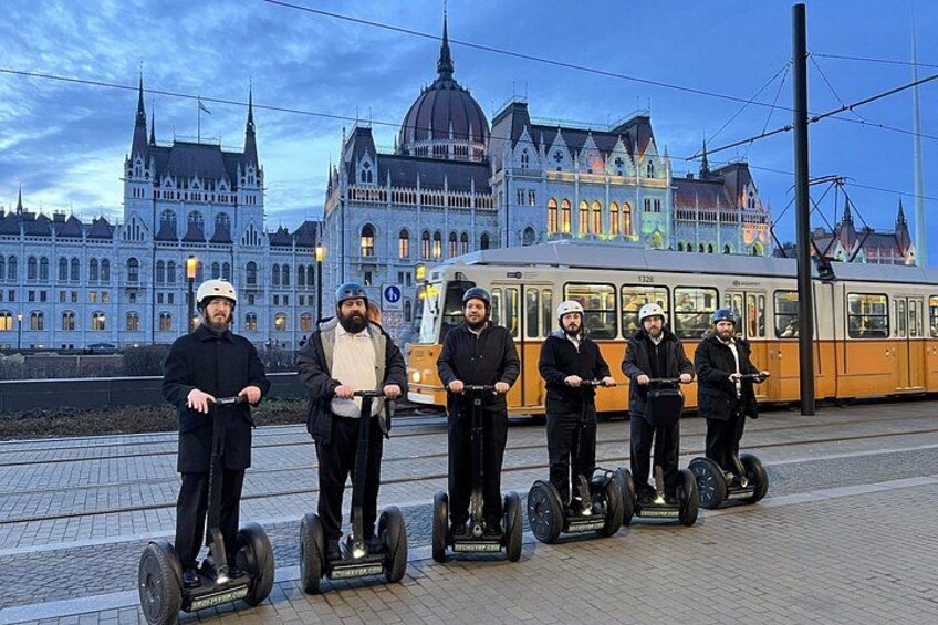 En grupp människor på segways framför en historisk byggnad, med en spårvagn i bakgrunden. 4