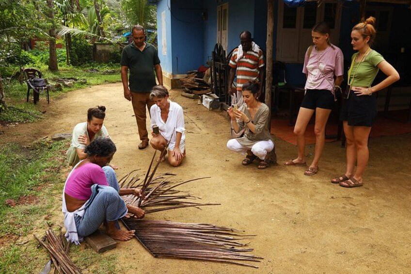 A group of people outdoors, some sitting and others standing, with a dirt ground and greenery in the background. 3