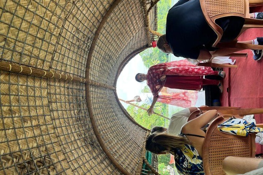 A covered outdoor area with a woven roof, chairs, and a person standing near the entrance. 2