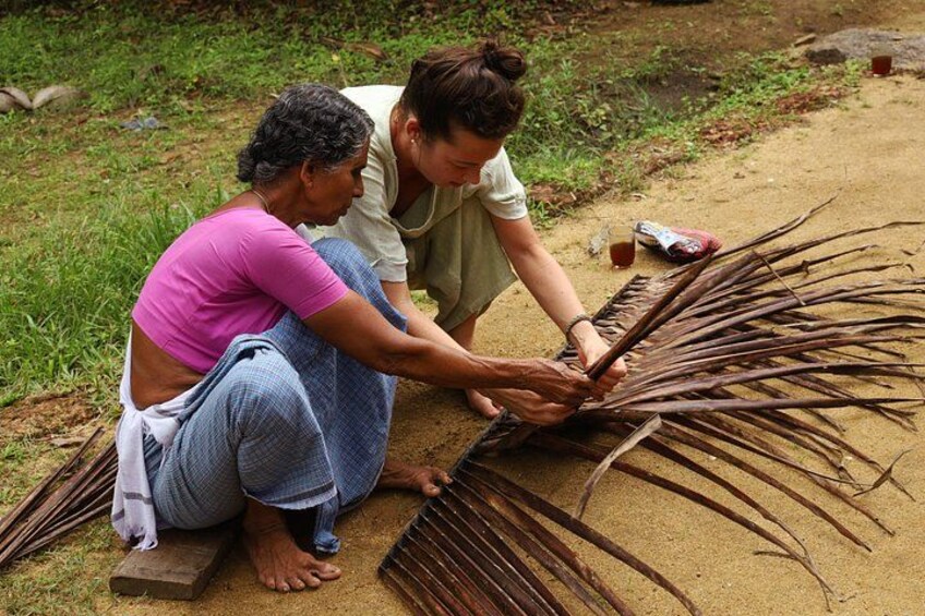 Two people sitting on the ground, working with long, thin branches. 2