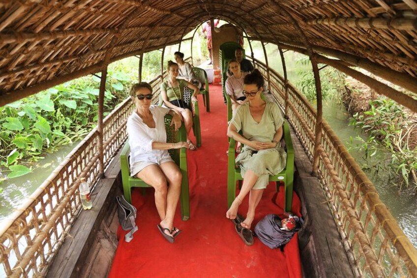 A covered wooden boat with passengers seated on green chairs. 1