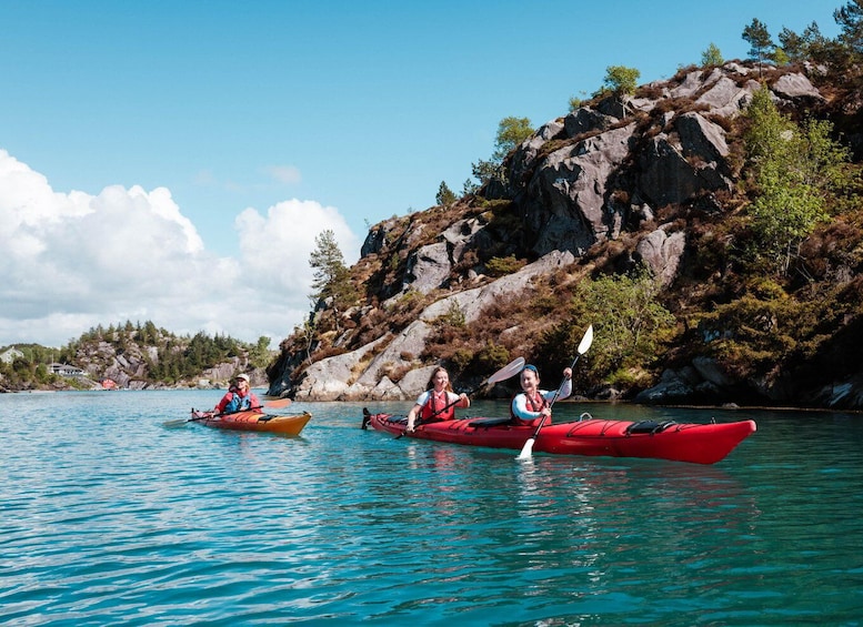 Three kayakers on a calm lake with rocky cliffs and sparse vegetation in the background. 1