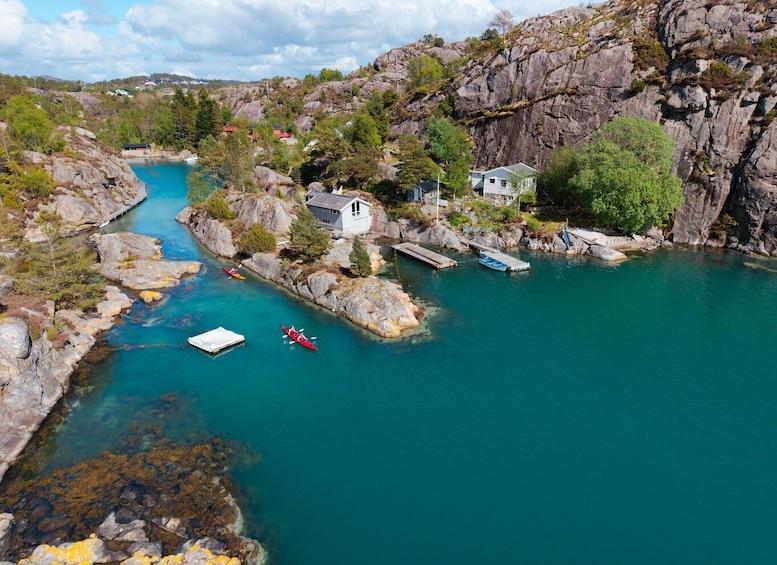 A river with kayaks, a dock, and houses on a rocky shore. 3