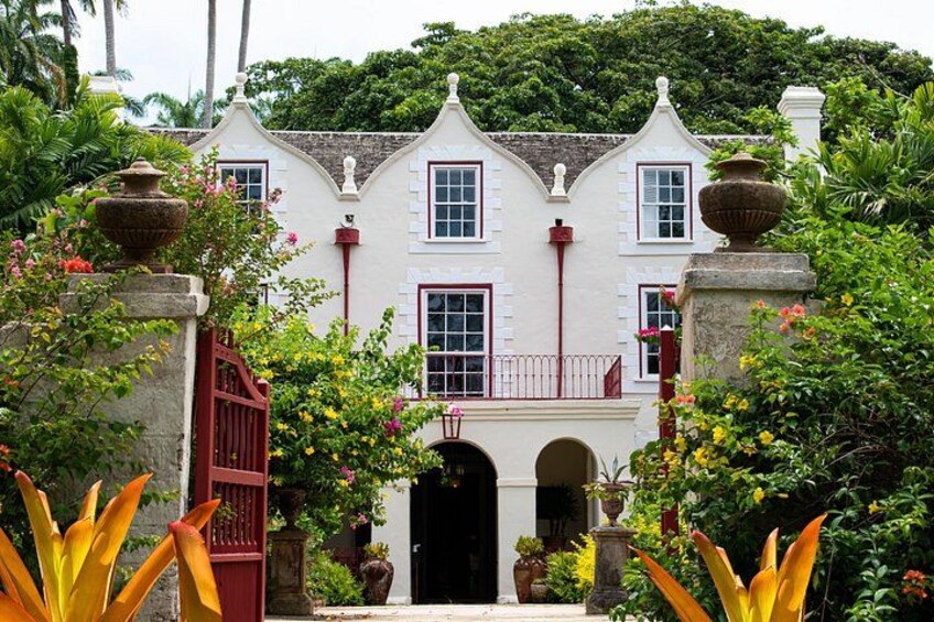 A colonial-style building with a white facade, red accents, and a lush garden. 1