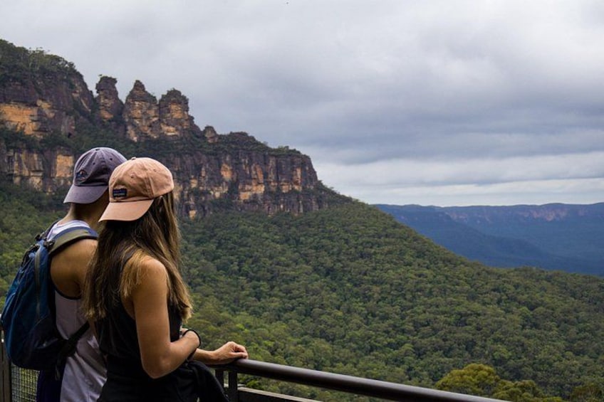 Two people sitting on a railing overlooking a forested mountain range. 4