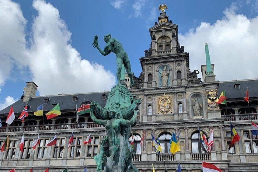 A historic building with a statue in front, flags, and a clear sky. 4