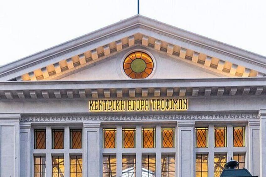 A building with a triangular pediment and a circular window. The text on the pediment reads "KENTRIKH ATORA TROFIMON". 1
