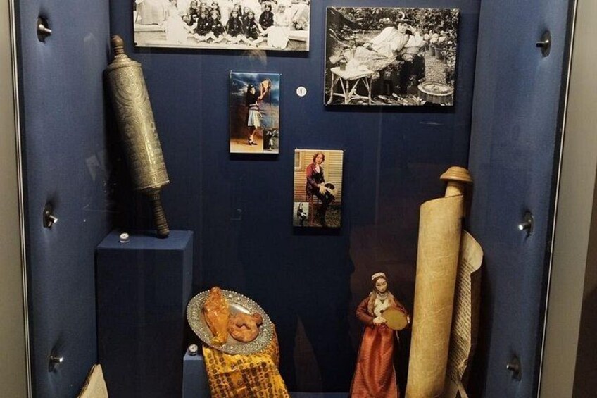 En udstillingsmontre med historiske fotografier, en rok og en statue. 3