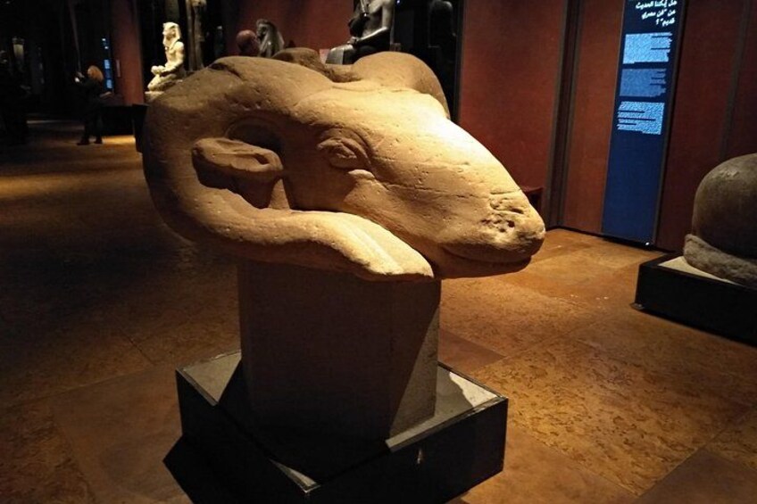 A stone sculpture of a ram's head on a pedestal in a museum. 2