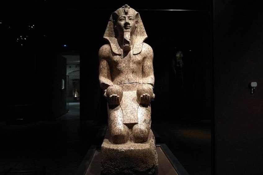 A stone statue of a seated figure with a headdress, in a dimly lit museum setting. 3