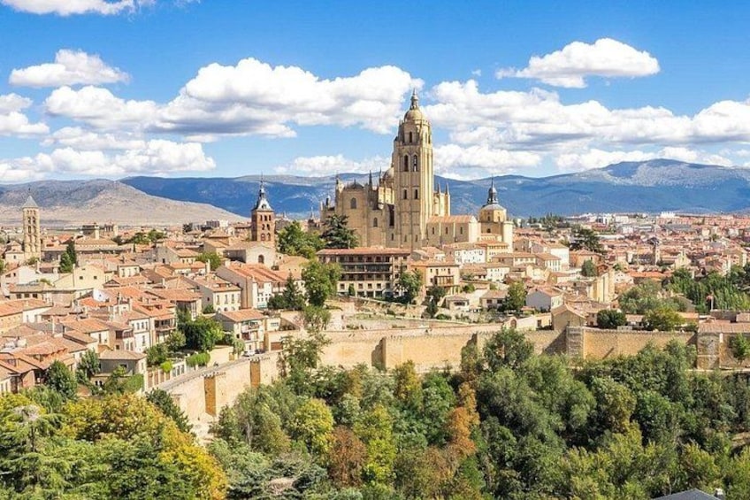 Un paysage urbain historique, dominé par une cathédrale imposante, des bâtiments environnants et un décor de montagnes en arrière-plan. 1